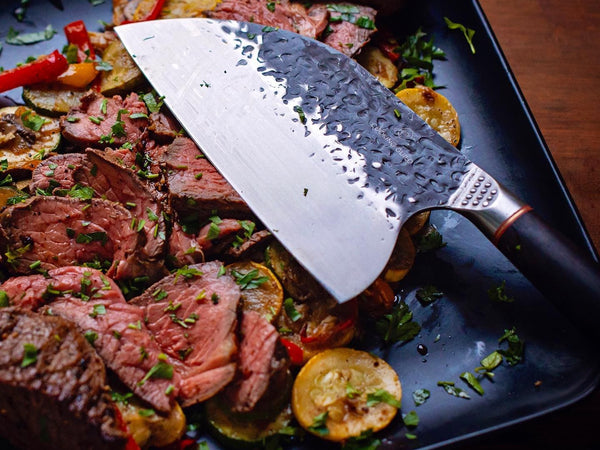 BBQ knives laid out for grilling — slicer, butcher knife and cleaver on a board