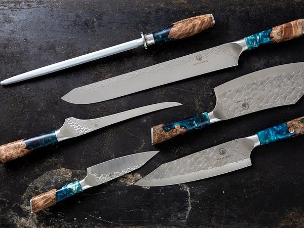 A group of hand-forged kitchen knives from a Cooking Guild knife set laid out on a dark surface